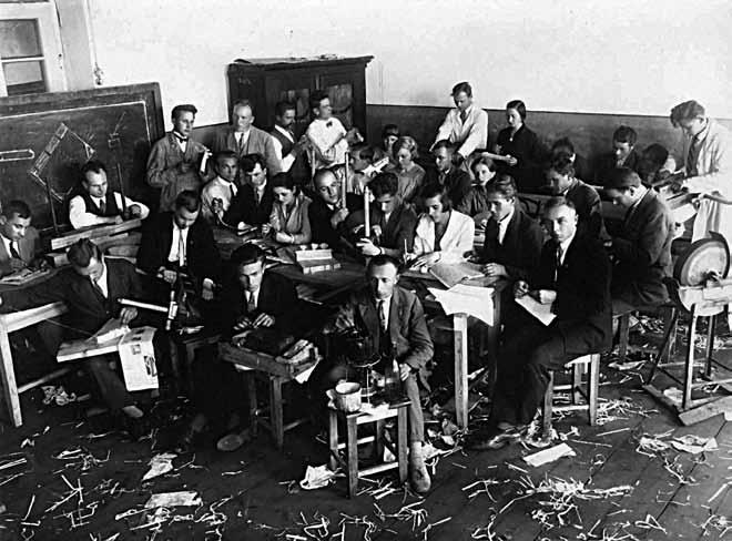 Pedagoginių darbo kursų dalyviai. Knygrišystės darbai. Šalia spintos stovi kursų vedėjas ir dėstytojas Antanas Vokietaitis. Ukmergė, 1930 m. priduoda kažkokio vaikiško gerumo. Vis susičiaupęs, rimtas.